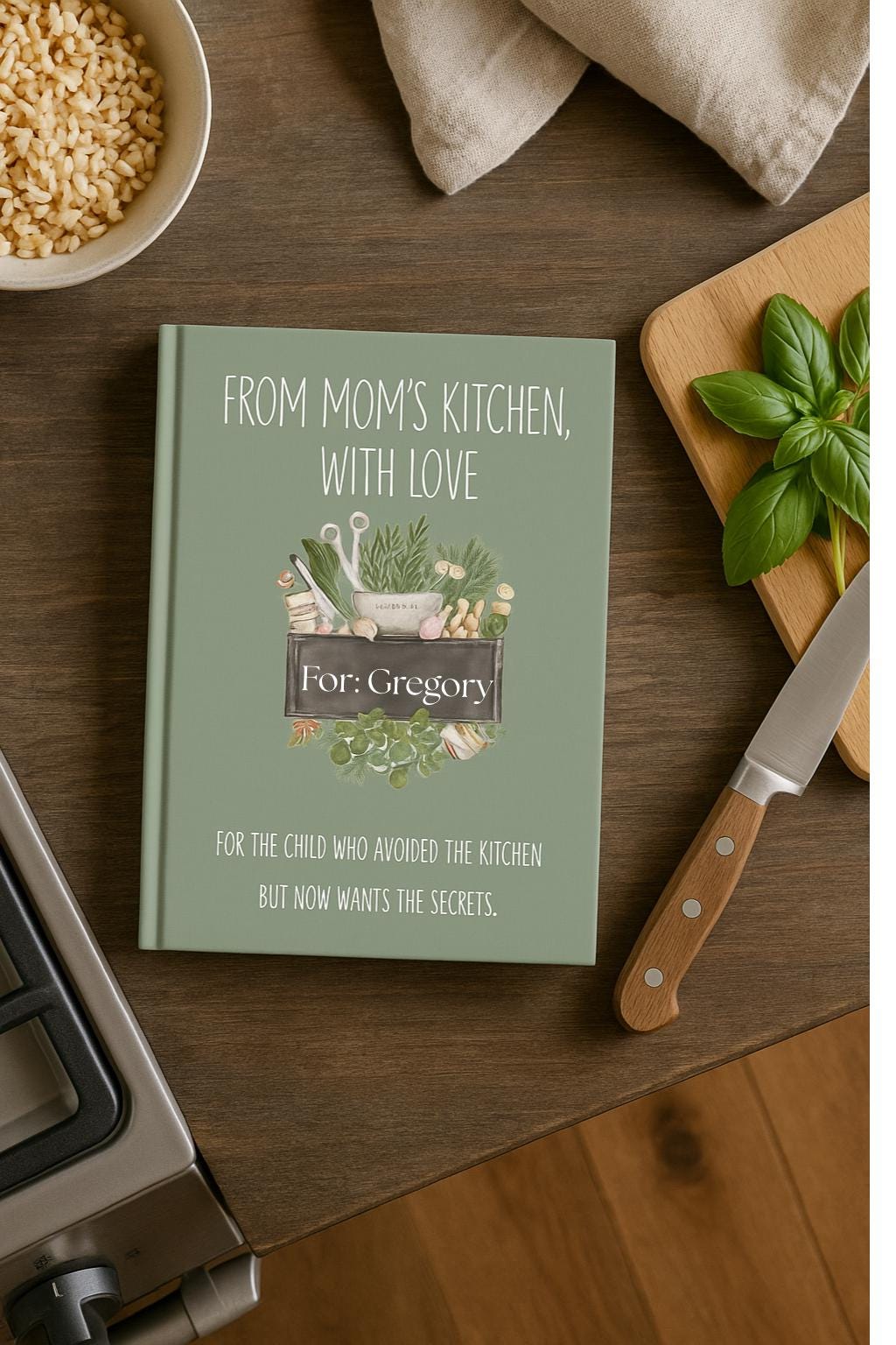 Sage green recipe legacy notebook titled ‘From Mom’s Kitchen, With Love’ on a rustic kitchen counter. Styled with fresh basil, cutting board, knife, and grains for a warm cooking vibe. Perfect personalized cookbook gift for family recipes.