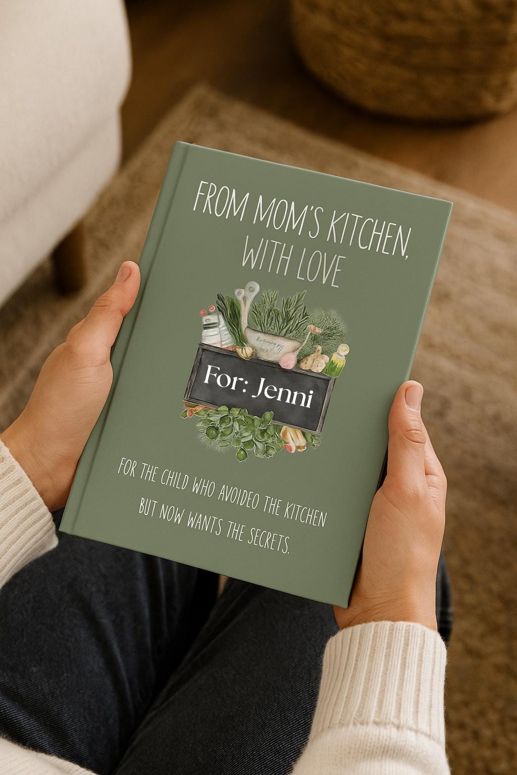 Personalized recipe legacy notebook with sage green cover titled ‘From Mom’s Kitchen, With Love.’ Shown in-hand, gently held by a person in a cozy cream knit sweater. Perfect sentimental gift for family recipes and kitchen keepsakes.
