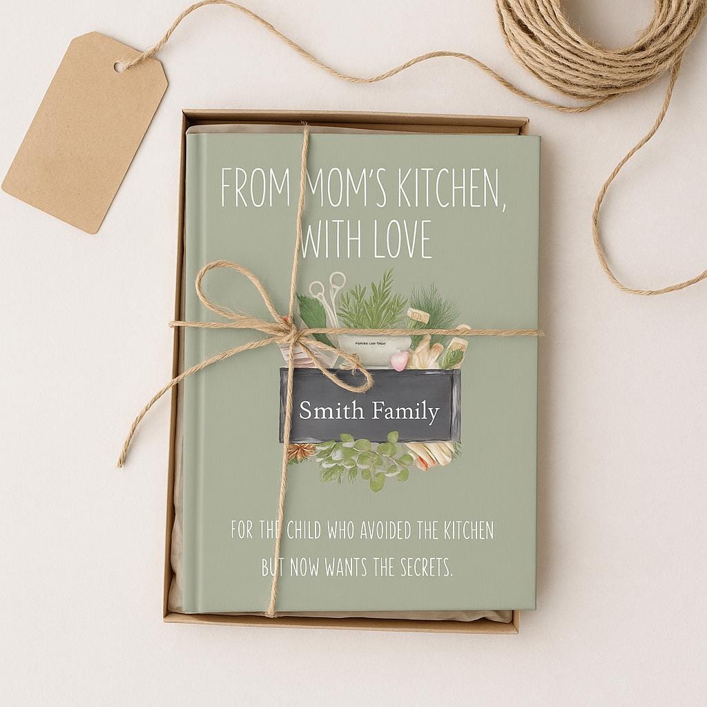 Gift-ready personalized recipe legacy notebook with sage green cover titled ‘From Mom’s Kitchen, With Love.’ Chalkboard personalization reads ‘For: Ashley.’ Notebook wrapped in kraft paper and tied with rustic twine, creating a thoughtful keepsake cookbook gift.