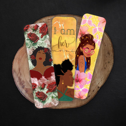 May include: Three bookmarks with different designs. The first bookmark has a red rose floral design with a black woman in a red dress. The second bookmark has a yellow background with the text &#39;i am her&#39; and a black woman with an afro. The third bookmark has a yellow background with pink flowers and butterflies and a black woman with long braids and glasses.